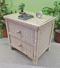 a white wicker chest with two drawers and a clock on top, next to potted plants