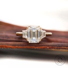 an emerald - cut diamond ring sits on top of a piece of wood