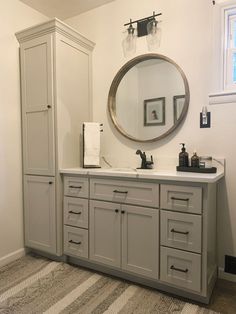 a bathroom with a large round mirror above the sink and gray cabinets on both sides