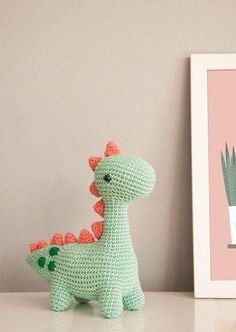 a crocheted toy dinosaur next to a framed photograph on a shelf with a plant