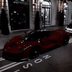 a red sports car is parked in front of a building with two cars on the street