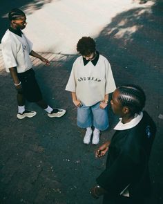 three people standing on the street talking to each other and one is wearing a white shirt