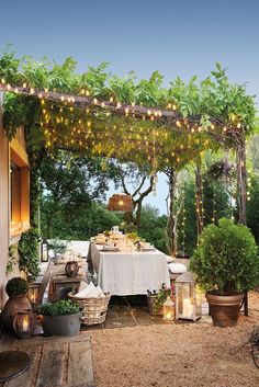 an outdoor dining area with potted plants and lights strung from the pergolated arbor