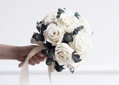 a bridal bouquet with white roses and greenery is being held by someone's hand