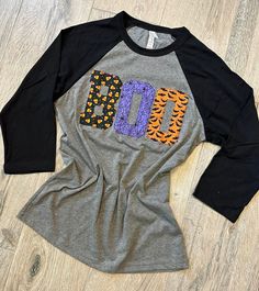 Super soft unisex sized tee in gray with black 3/4 baseball sleeves. The design is the word BOO in cotton candy corn, purple spider web, and orange bat fabric. This is a  Bella/Canvas tee that is 52% cotton and 48% polyester so it is really soft and light weight.  I sew the letters on with a regular sewing machine-not an embroidery machine, so there is no heavy thick backing on the inside of the shirt. Just lightweight and comfortable.  small  med  large  XL  2XL  These shirts are unisex and fit true to size.  For best results, machine wash gentle cycle and lay flat to dry. **Remember, my items are stitched on the garment with a zig zag stitch in most cases; therefore, the fabric will fray around the edges. This is what they are supposed to do. If you don't like some of the longer strings Purple Spider, Zig Zag Stitch, Bats Halloween, Cross Shirts, Bella Canvas Tees, Halloween Bats, Halloween Tees, Two Girls, Candy Corn