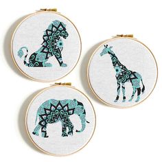 three cross stitch hoops with an elephant and giraffe in blue on them