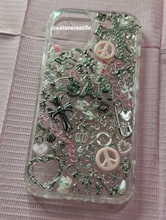 an iphone case with buttons and charms on it sitting on a pink cloth covered surface