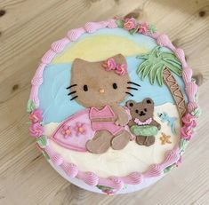 a hello kitty cake with a teddy bear and palm tree on the top, sitting on a wooden table