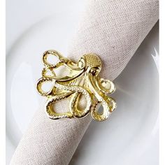 an octopus napkin holder on top of a white plate with a gold colored napkin ring