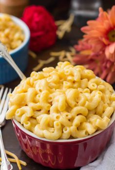 a bowl filled with macaroni and cheese on top of a table next to flowers