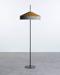 a floor lamp with a gold shade on the top and fringed lampshade