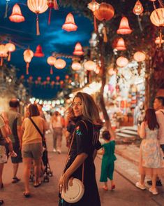 a woman standing in the middle of a crowded street with lanterns hanging from the ceiling