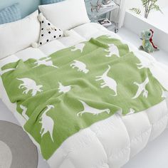 a green and white dinosaur blanket on top of a bed in a child's bedroom