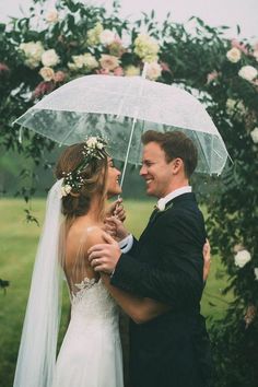 a bride and groom standing under an umbrella in front of a floral arch at their wedding