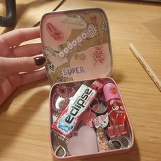 a pink box filled with assorted items on top of a wooden table next to a person's hand