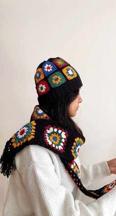 a woman wearing a knitted hat and scarf is looking at something on the wall