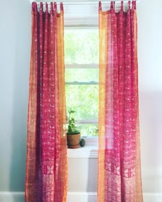 an orange and pink curtain hangs in front of a window with potted plants on the ledge