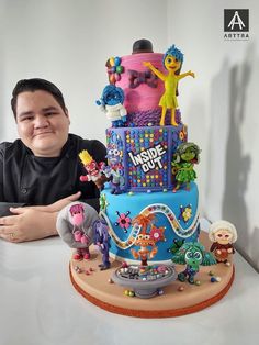 a man sitting in front of a large cake with cartoon characters on it and an inside out sign