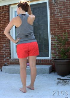 a woman standing in front of a brick building with her back to the camera, wearing red shorts