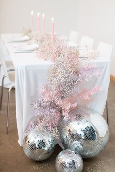 silver disco ball centerpieces on a white tablecloth with pink flowers and candles