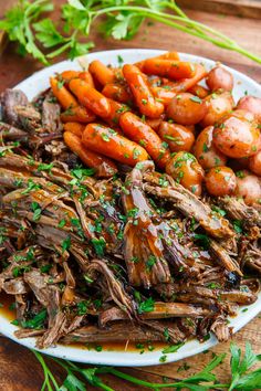 a white plate topped with meat and carrots next to green garnish on top of a wooden table