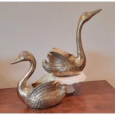 two metal birds sitting on top of a wooden table