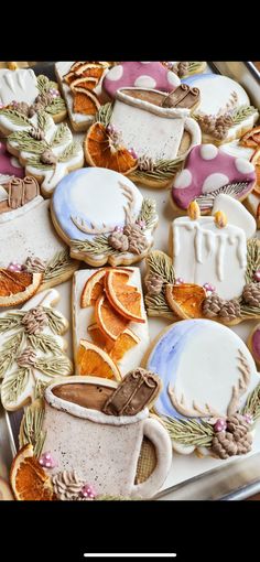 decorated cookies in the shape of coffee cups and oranges on a tray with leaves