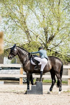 a woman riding on the back of a brown horse next to a wooden fence and trees