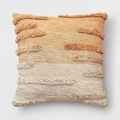 an orange and beige pillow with fringes on the front, sitting against a white wall