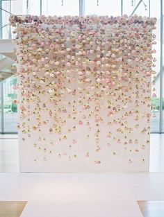 a large white sculpture with pink and yellow flowers hanging from it's sides in front of a glass wall