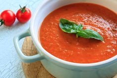 a bowl of tomato soup with basil on the top and tomatoes in the back ground