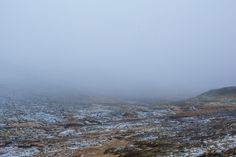 an open field covered in lots of snow next to a hill on a foggy day