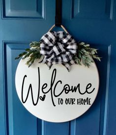 a welcome to our home sign hanging on a blue door with a black and white bow