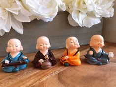 four small buddha figurines sitting on a wooden table next to white flowers in a vase