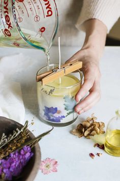 a person pouring some kind of liquid into a glass container with flowers on the table next to it