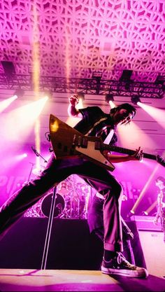 a man on stage with his guitar in the air and purple lighting behind him,