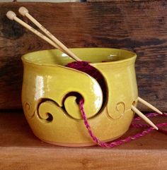 a yellow bowl with two knitting needles in it