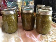 four jars filled with pickles sitting on top of a table next to a stove