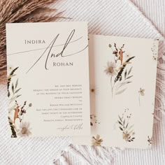 the wedding stationery is laid out on top of a white blanket with flowers and greenery