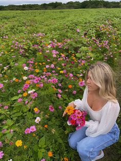 a woman kneeling down in a field full of flowers