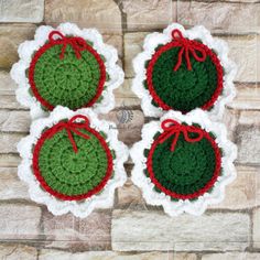 four crocheted christmas ornaments with red and green trim on them sitting next to a brick wall