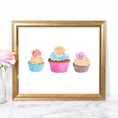 three cupcakes are sitting on a table next to a vase with pink flowers