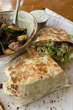 a white plate topped with a burrito next to a bowl of salad