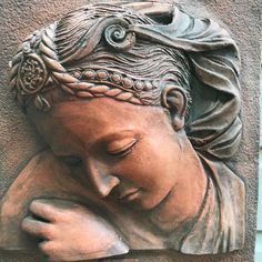 a statue of a woman with her head resting on her hand, against a stone wall