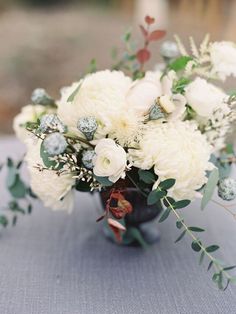 a vase filled with white flowers and greenery on top of a table covered in blue cloth