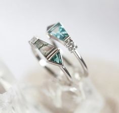 two silver rings with blue and green stones on them sitting on top of each other