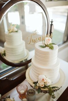 a white wedding cake sitting on top of a table next to a mirror and wine glasses