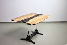 a wooden table sitting on top of a black metal stand up leg next to a white wall