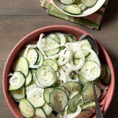 two bowls filled with cucumbers and onions on top of a wooden table next to silverware