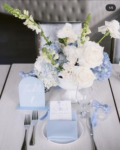 a table set with blue and white flowers, napkins, silverware and place settings